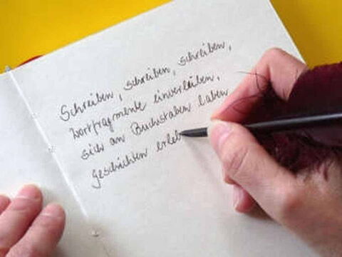 Foto: Jemand schreibt mit Tinte und einer Gänsefeder einen Text in ein leeres Buch.