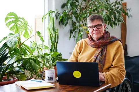 Foto: Andrea tippt Texte in ihren Laptop. Im Hintergrund sind viele Pflanzen zu sehen.