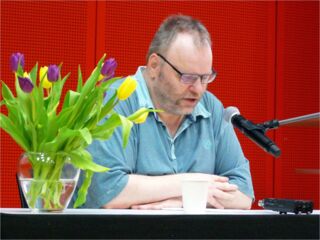 Foto: Hier bin ich im Halbprofil mit einem Strauß bunter Tulpen am linken Bildrand beim Vorlesen zu sehen.
