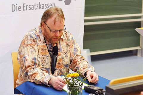 Foto: Hier seht ihr mich während der Lesung in meine Texte vertieft. Im Hintergrund ein Banner der Ersatzkassen.