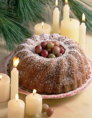 Foto: Ein brauner Marmorkuchen zwischen brennenden Kerzen unter einem Baum.