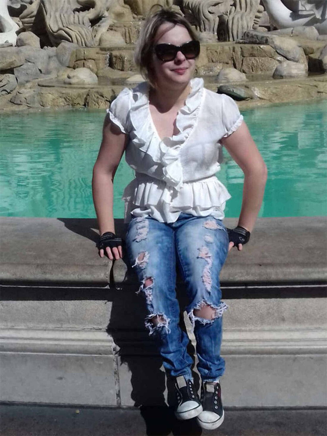 Foto: Akimaus in weißer Rüschenbluse und blauer zerrissener Jeans auf einem Brunnenrand in Las Vegas.