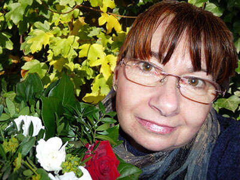 Foto: Bribri mit einem Rosenstrauß vor einer großen Hecke.