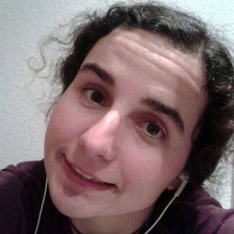 Foto: Portrait von Mio in einem Lila Pullover mit zwei weißen Ohrhörern.