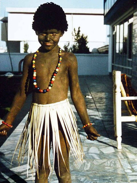 Foto: Ich bin komplett braun bemalt, trage nur ein Baströckchen und eine bunte Perlenkette um den Hals.