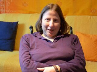 Foto: Evelyn als Portrait mit einem lila Hemd vor meinem gelben Sofa in meinem Snoozleraum.