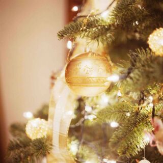 Foto: Goldene Kugeln und Kerzen leuchten am Weihnachtsbaum.
