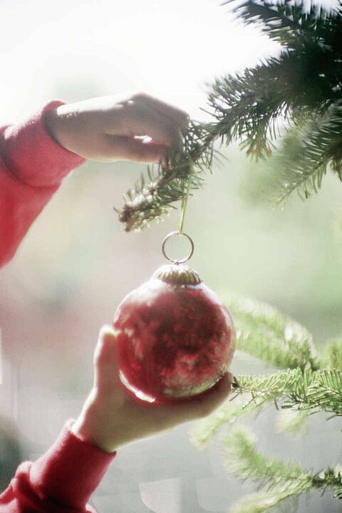 Foto: Ein Kind hängt eine rote Weihnachtskugel an einen Tannenbaum.