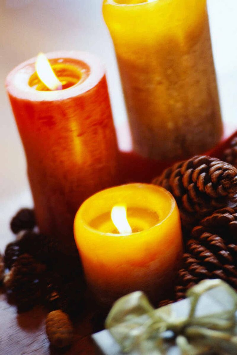 Foto: Drei brennende Kerzen zwischen Nüssen, Tannenzapfen und Geschenken.