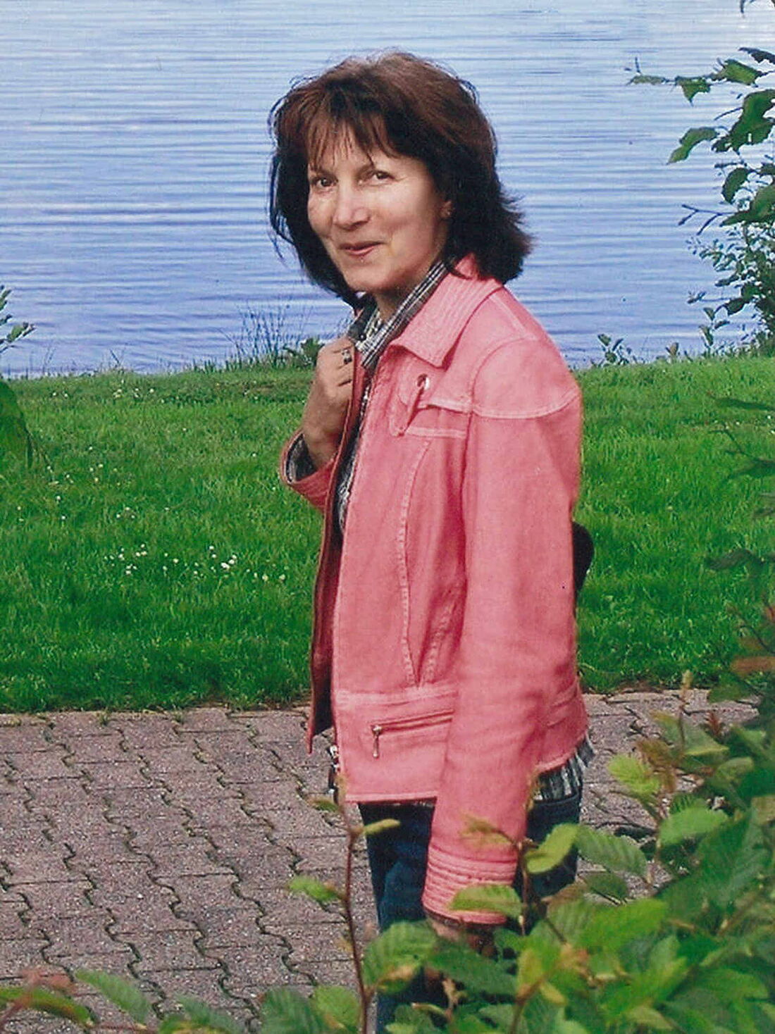 Foto: Renate in blauer Jeans und roter Jeans-Jacke schaut nach links in die Kamera und lächelt.