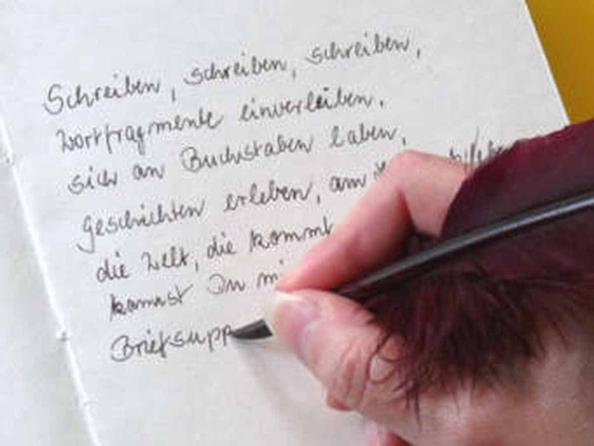Foto: Eine Schreibmaus schreibt mit Tinte und Feder einen Text in ein leeres Buch.