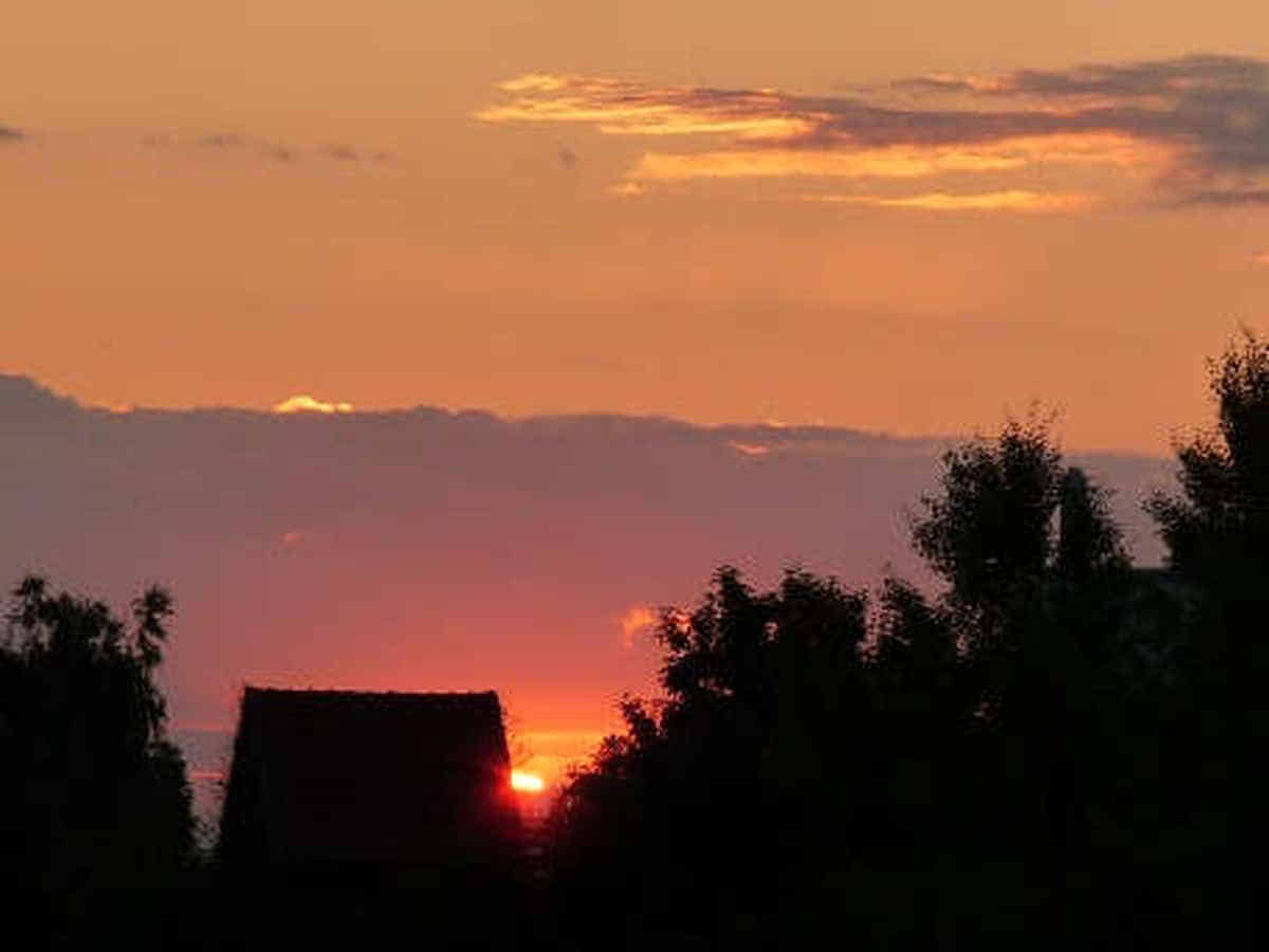 Foto: Die Sonne geht gerade hinter einer kleinen Hütte und Bäumen auf.